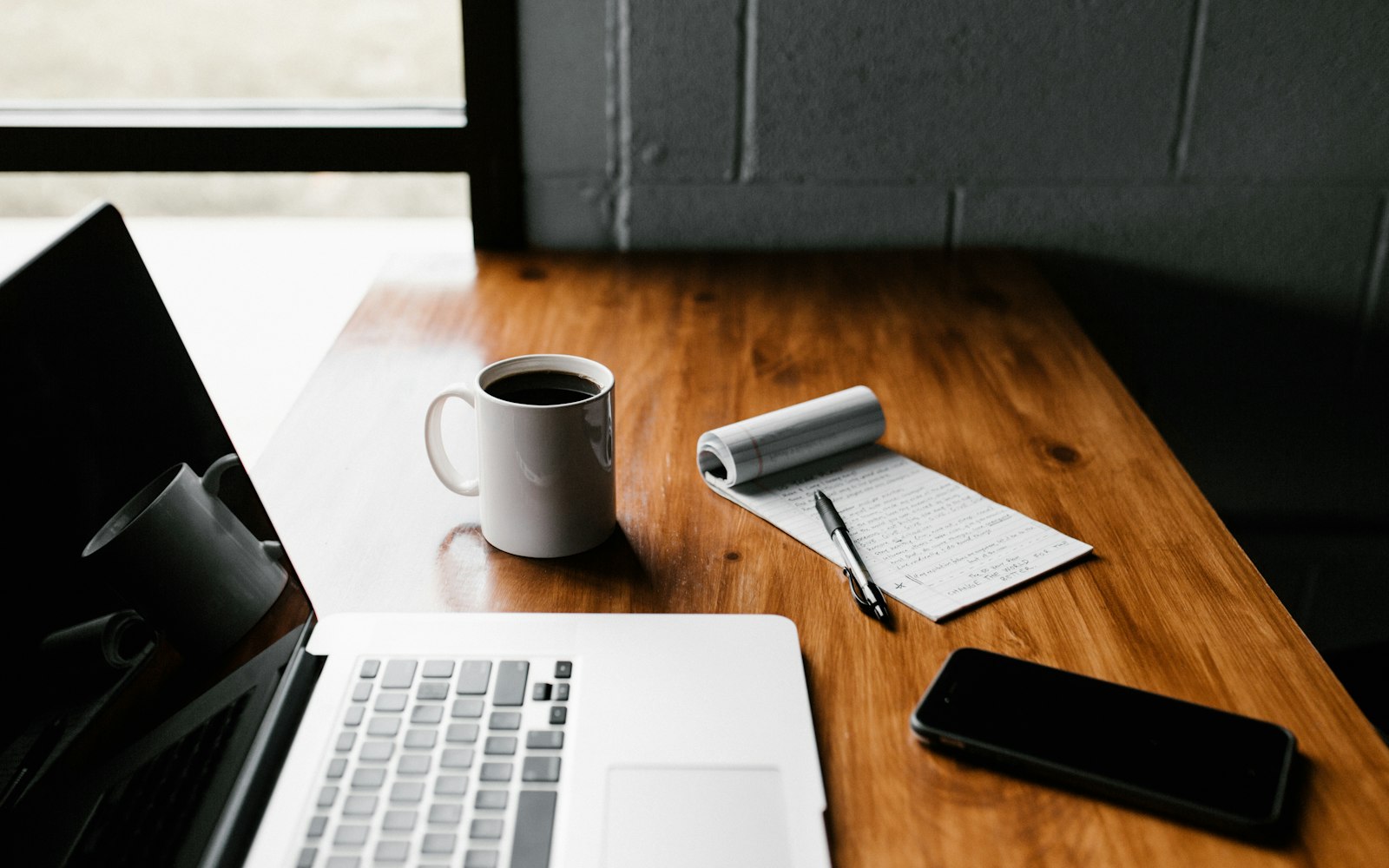 A laptop, coffee, and a notepad on a wooden desk